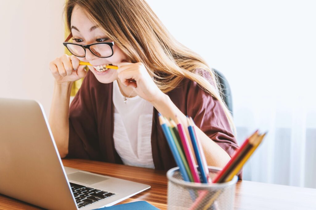 Woman biting a pencil, looking at laptop