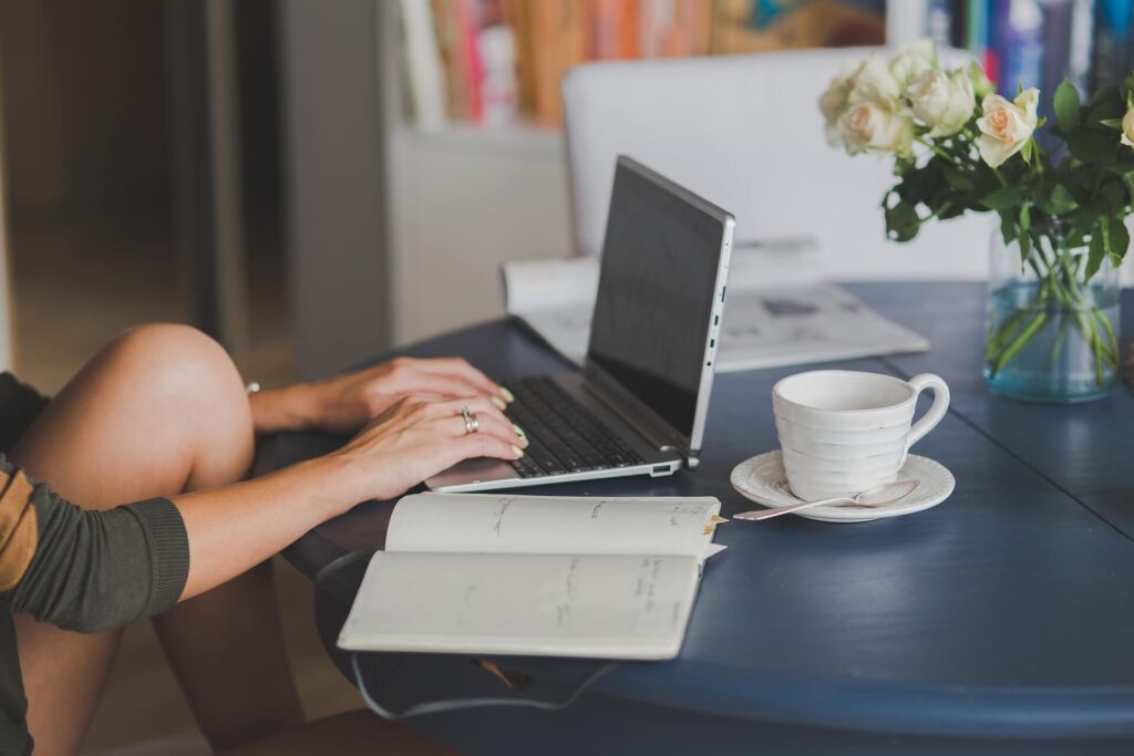 Freelancer working on laptop, table with coffee cup, notebook, and flower vase