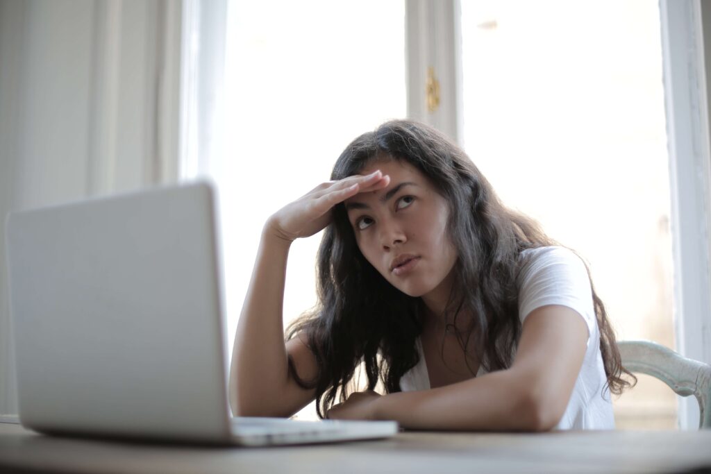 woman with hand on head, facing laptop