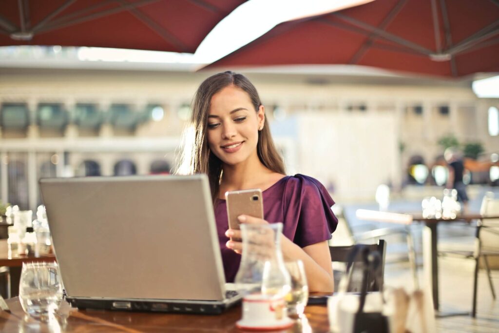 Woman with an open laptop, smiling at mobile phone