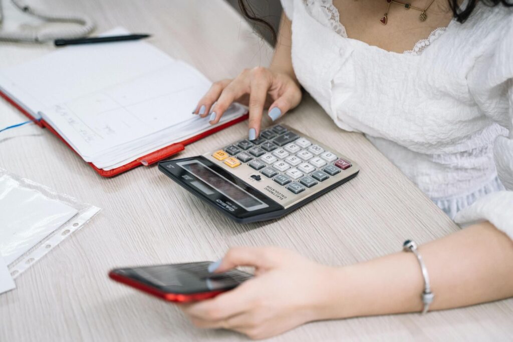 Woman using calculator and mobile phone, open notebook