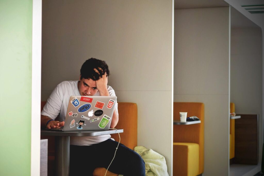 Man sitting down, facing laptop, one hand on head.