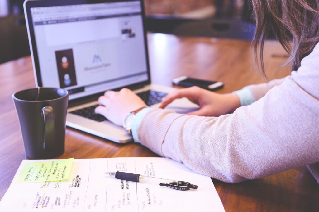 woman using laptop with paper and pen on table