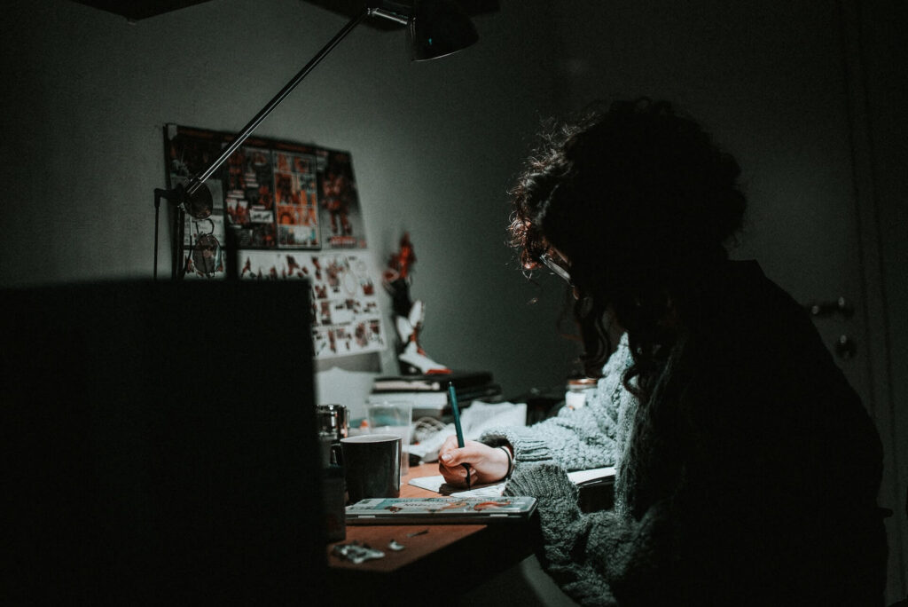 Artist drawing on table with lamp overhead to brighten dark room 