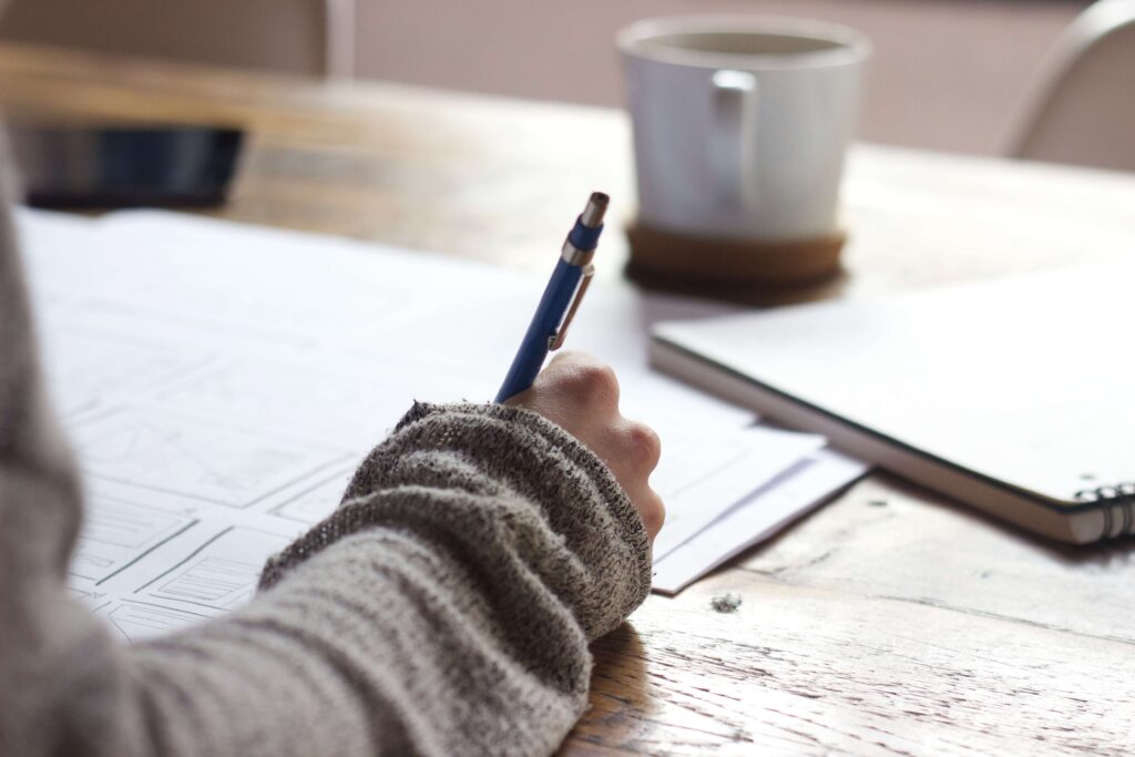 hand writing on paper with notebook and coffee on table