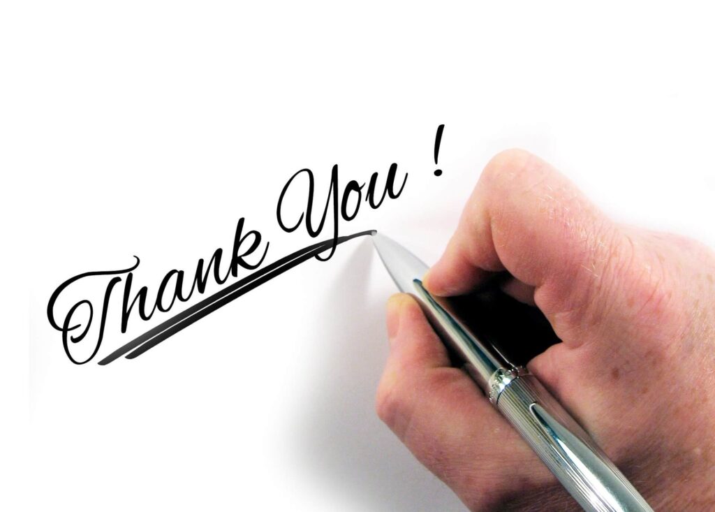 Hand holding a pen writing thank you with an underline underneath 