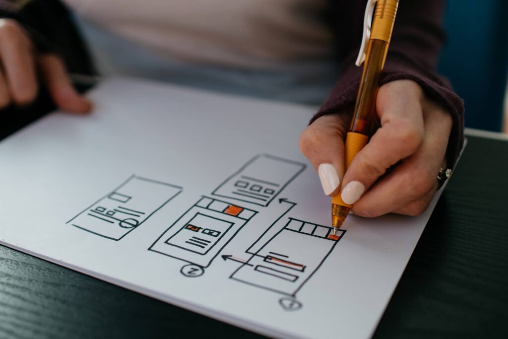 Person drawing workflow or wireframes on paper using an orange pen