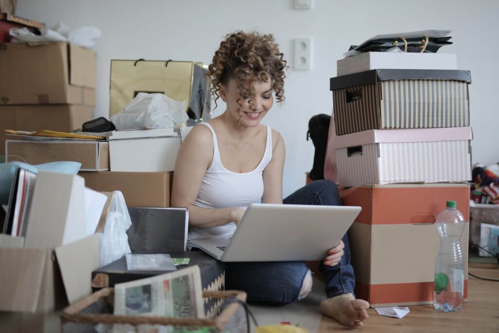 Woman sitting on the floor using a laptop surrounded by boxes