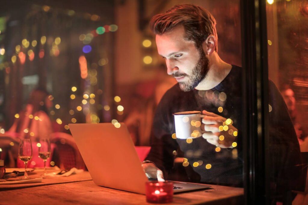 Man using a laptop in a restaurant, one hand holding a mug