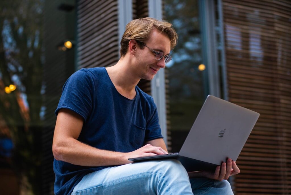 Man wearing glasses sitting down, smiling at laptop