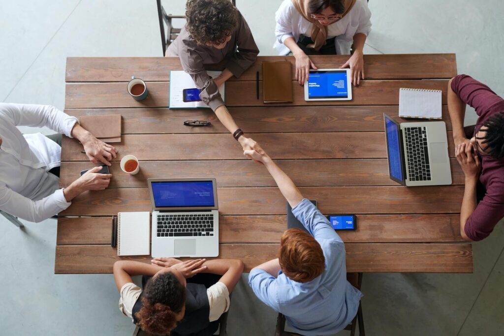 Top shot of table with 6 people, laptops and notebooks on top