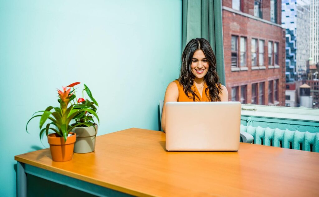 Woman smiling, sitting in front of a table, using a laptop