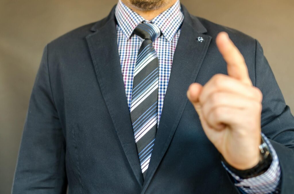 Man wearing a suit and tie, holding index finger up