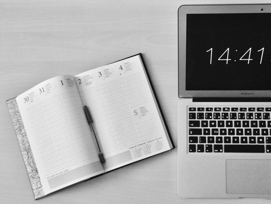 Open notebook planner with pen beside a laptop with time 14:41