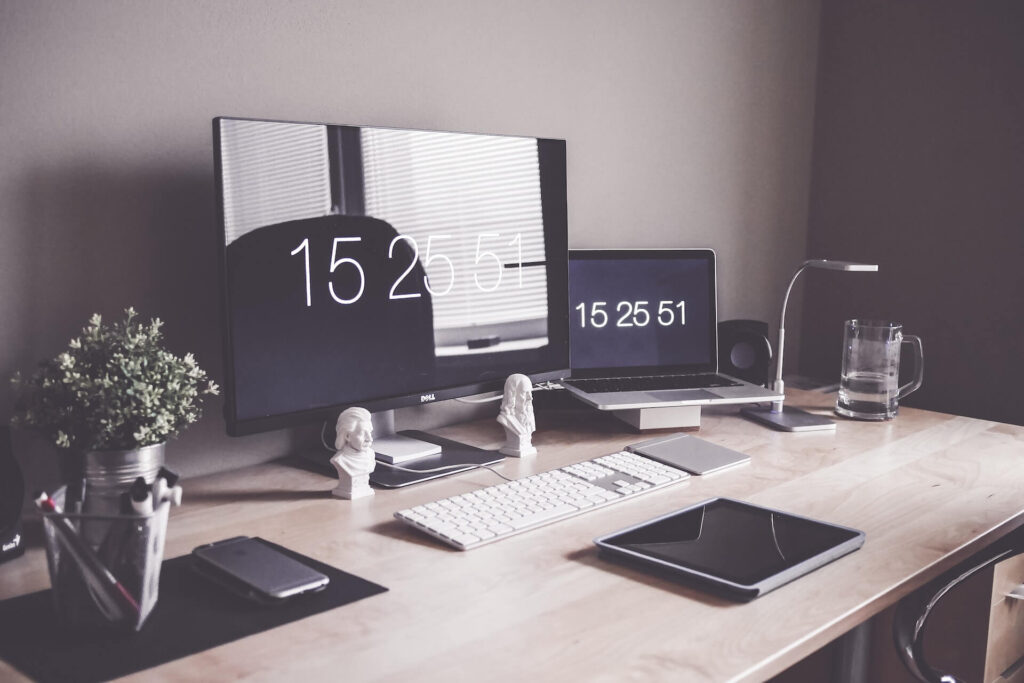 Full desk setup with monitor, laptop, speaker, small lamp, keyboard, trackpad, tablet, and mobile phone