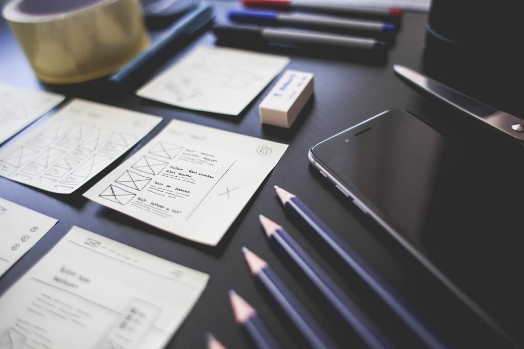 Drawing of website design on sticky notes placed on a table along with a mobile phone and pencils.