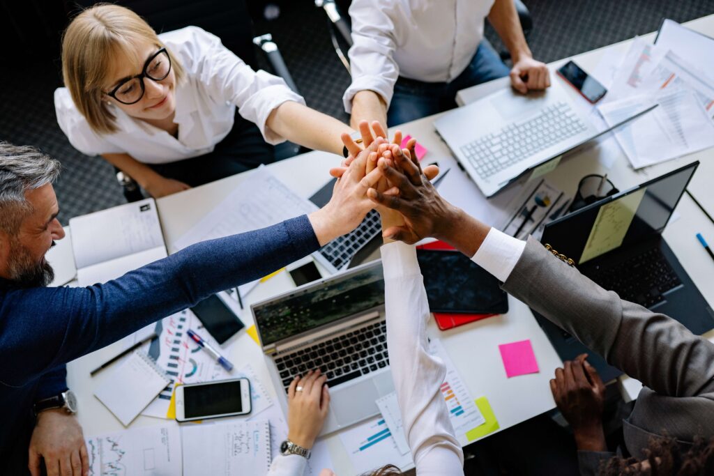 office team high five with laptops and files on table