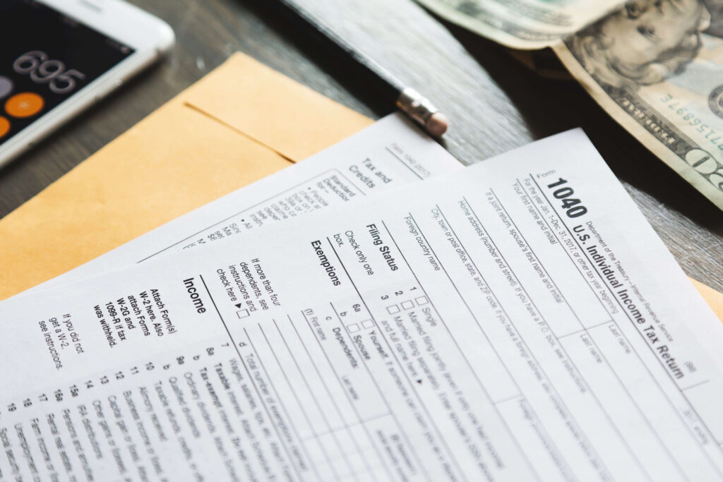 US tax forms on table crowded with a pencil, phone, and 20 dollar note
