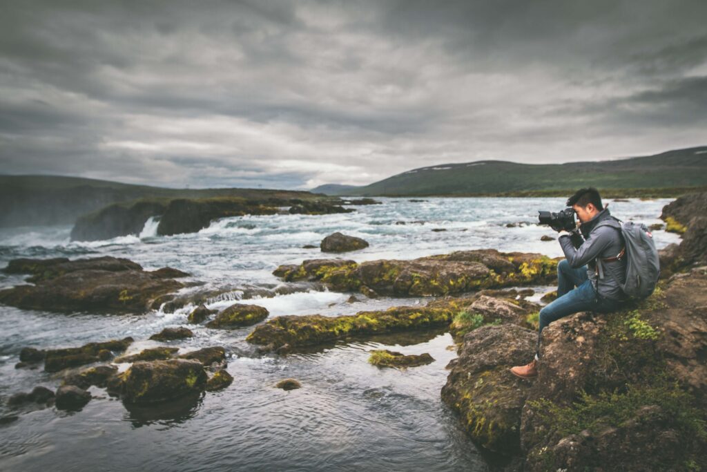 photographer sitting on rocks taking photo of a river