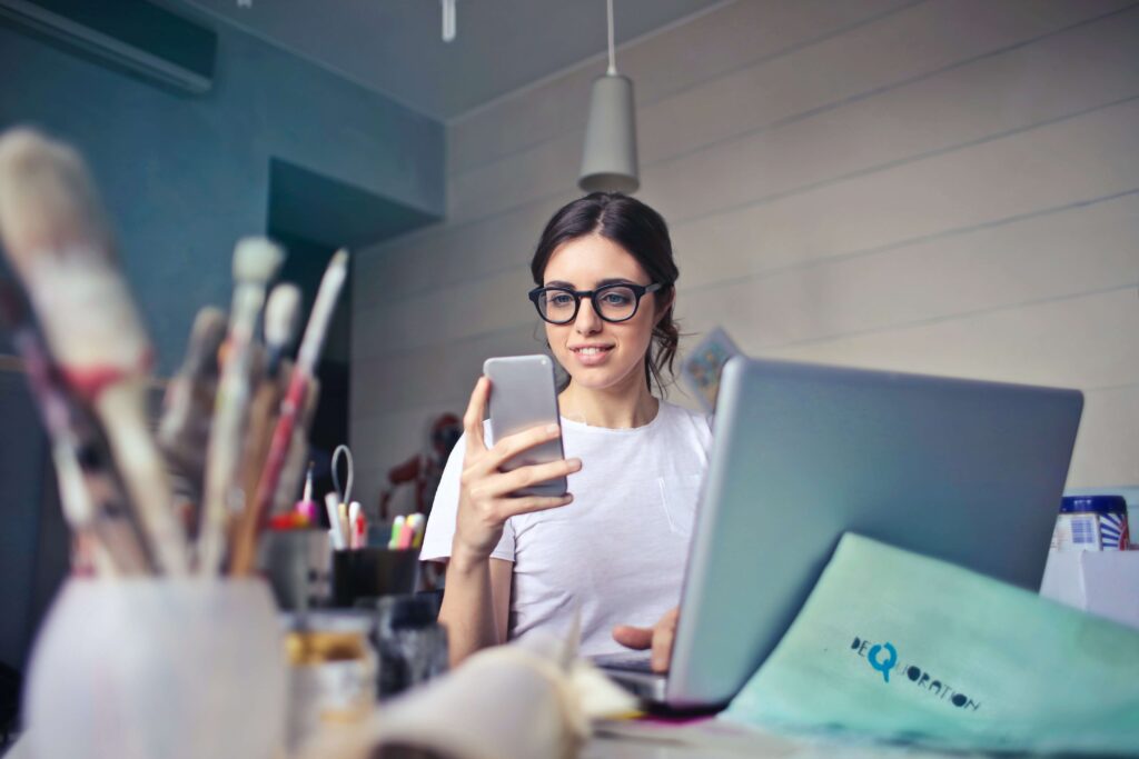 woman looking at phone with laptop on table