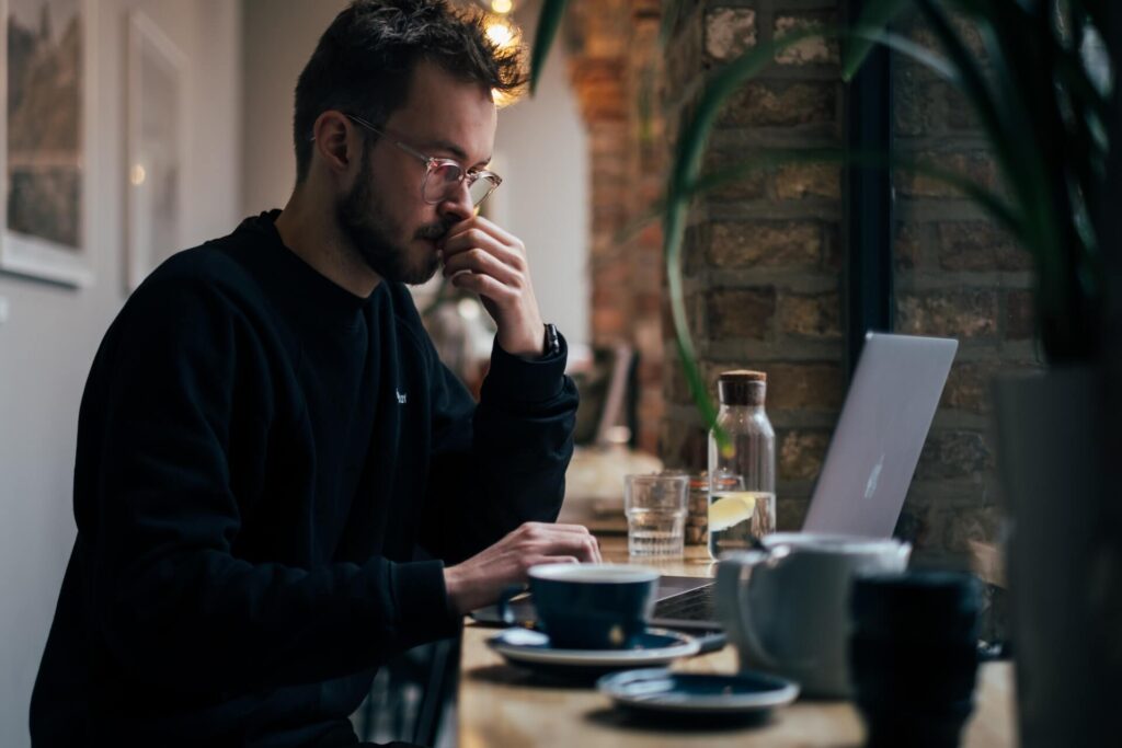 Man wearing glasses sitting on a bar using a laptop