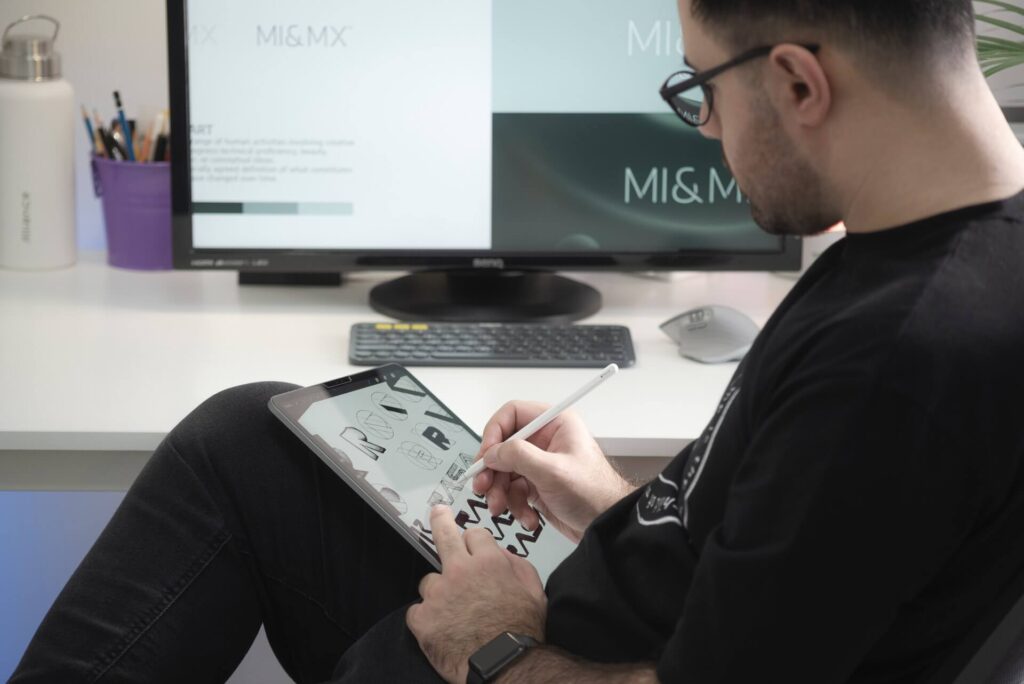 Man drawing on tablet, sitting in front of a large monitor.