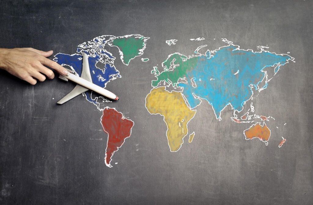 world map drawn on chalk with hand pushing a toy airplane