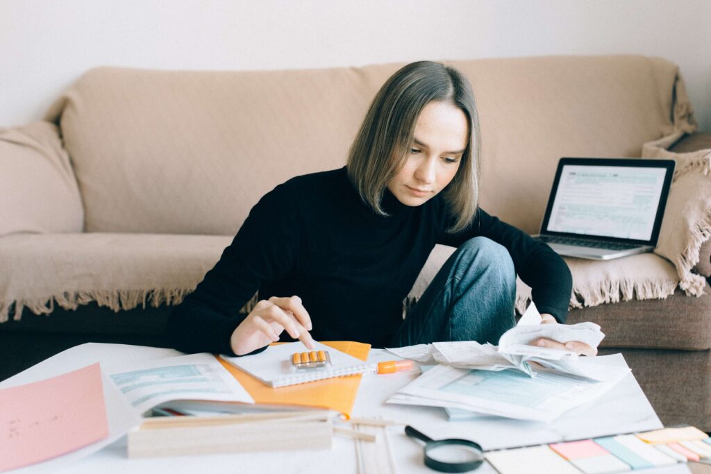 woman calculating with papers on table and laptop on couch background