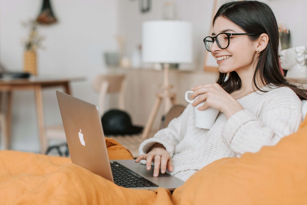 woman holding cup and smiling while looking at laptop