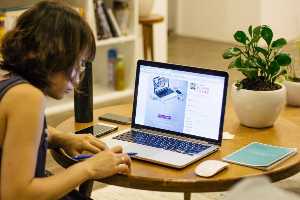 Woman sitting in front of desk that has a laptop, mouse, mobile phones, and a book.