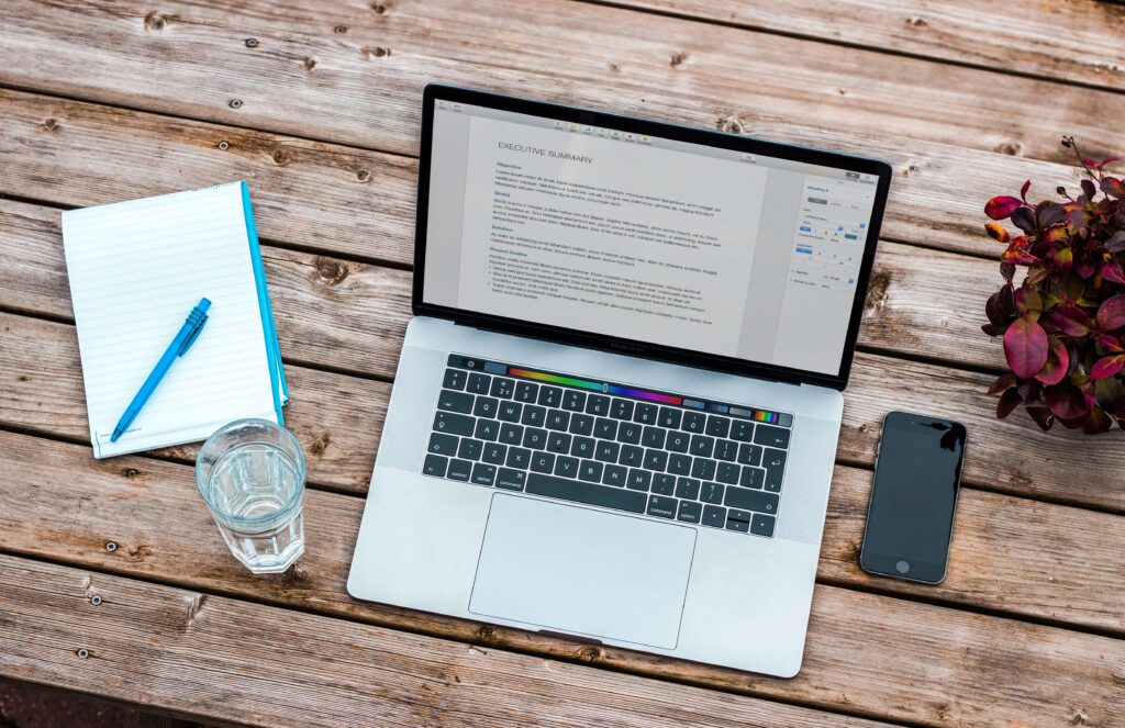 laptop, notepad with pen, iPhone on a table