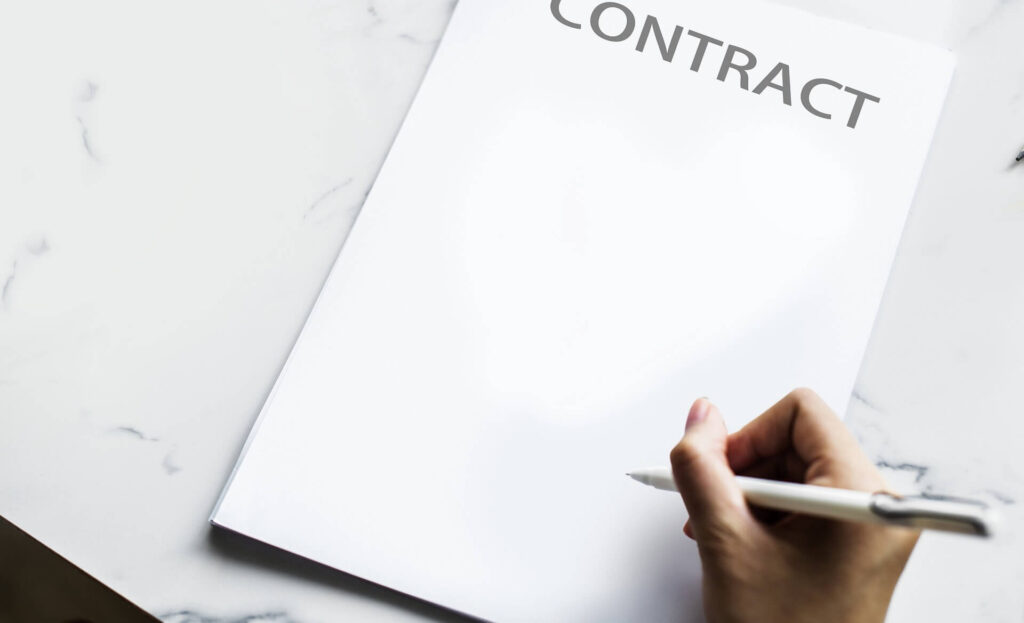 Blank paper with the word Contract on it, hand holding a pen 