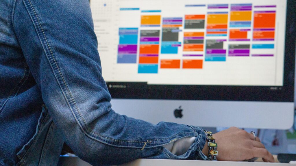 person's arm and iMac showing colored calendar of schedules