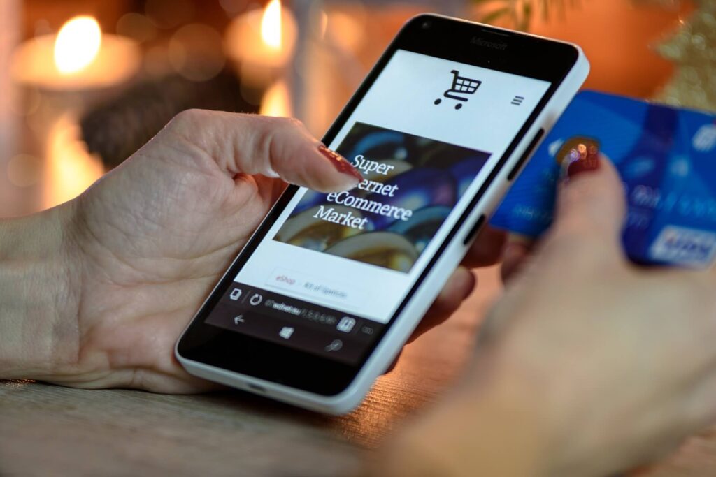 woman's hand holding blurred credit card and phone showing e-commerce page