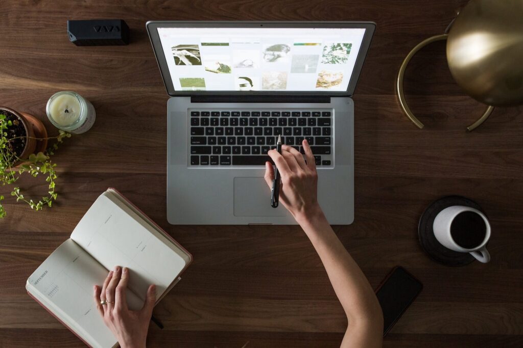 person typing on laptop with open notebook on the side