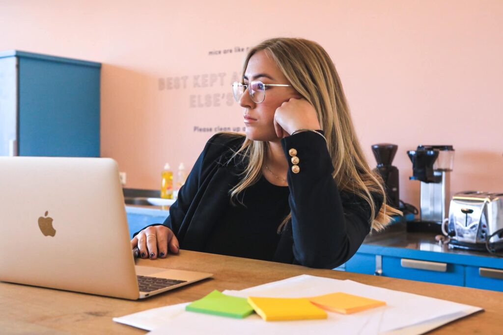 Woman in blazer, wearing glasses, thinking while using laptop