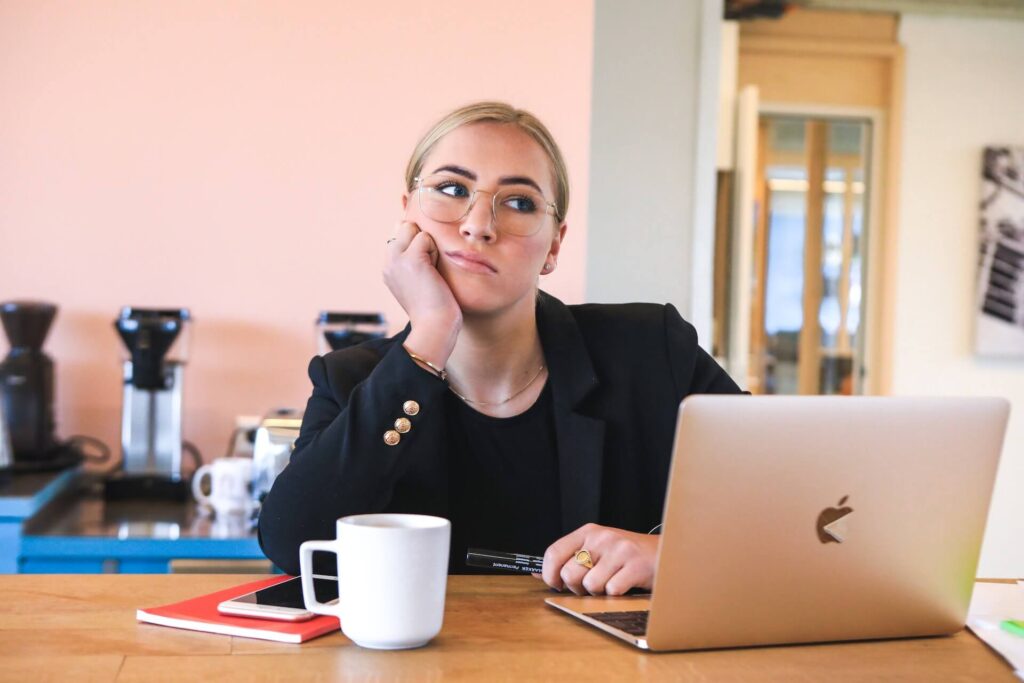 Woman thinking, open laptop in front of her