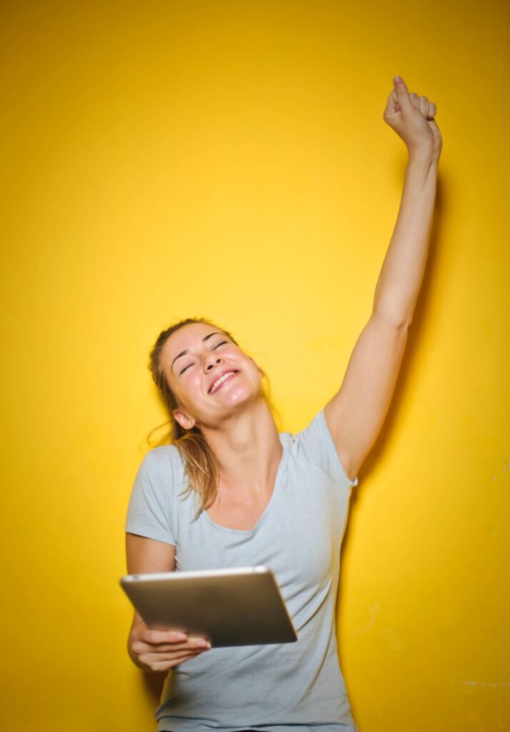 Woman with one arm up, smiling, holding an ipad with her other hand