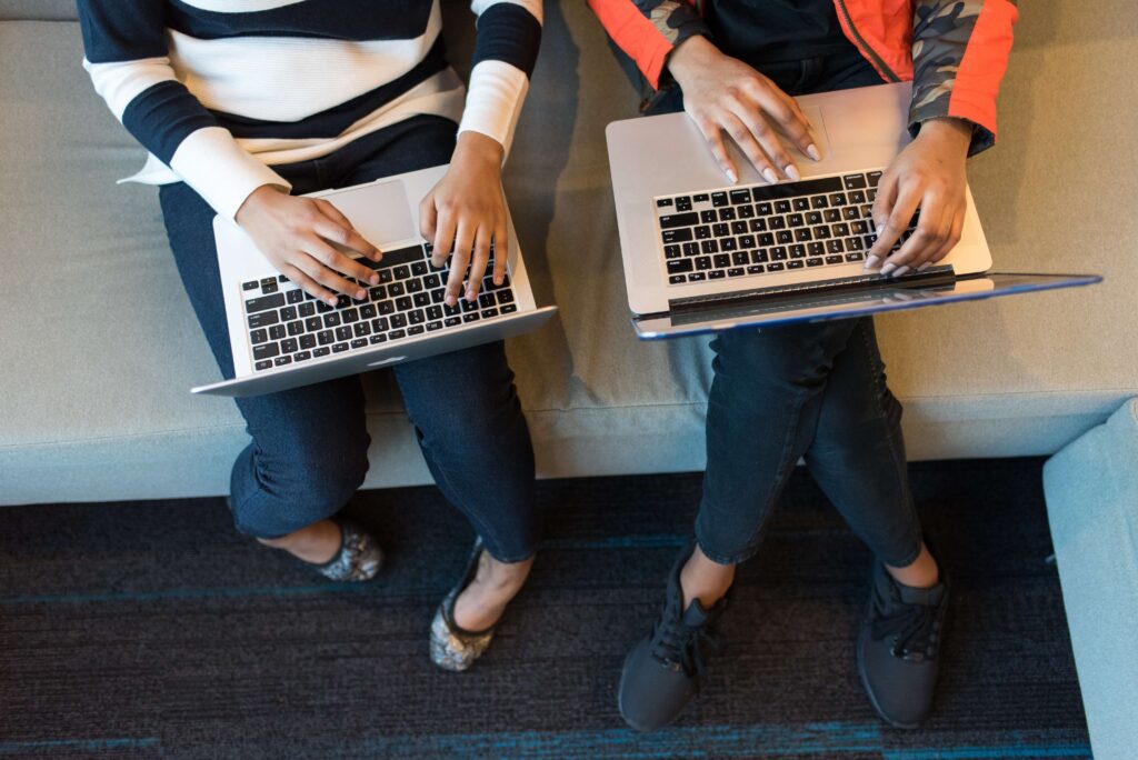 Top shot of two people sitting side by side, using laptops