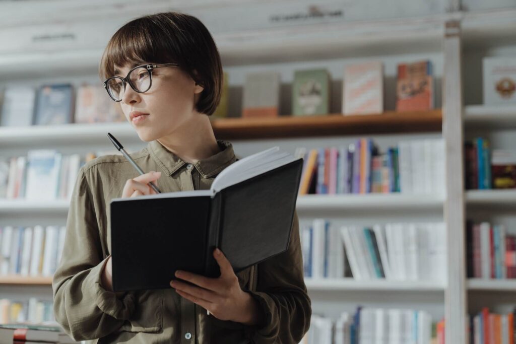 Woman wearing glasses, holding pen and open notebook