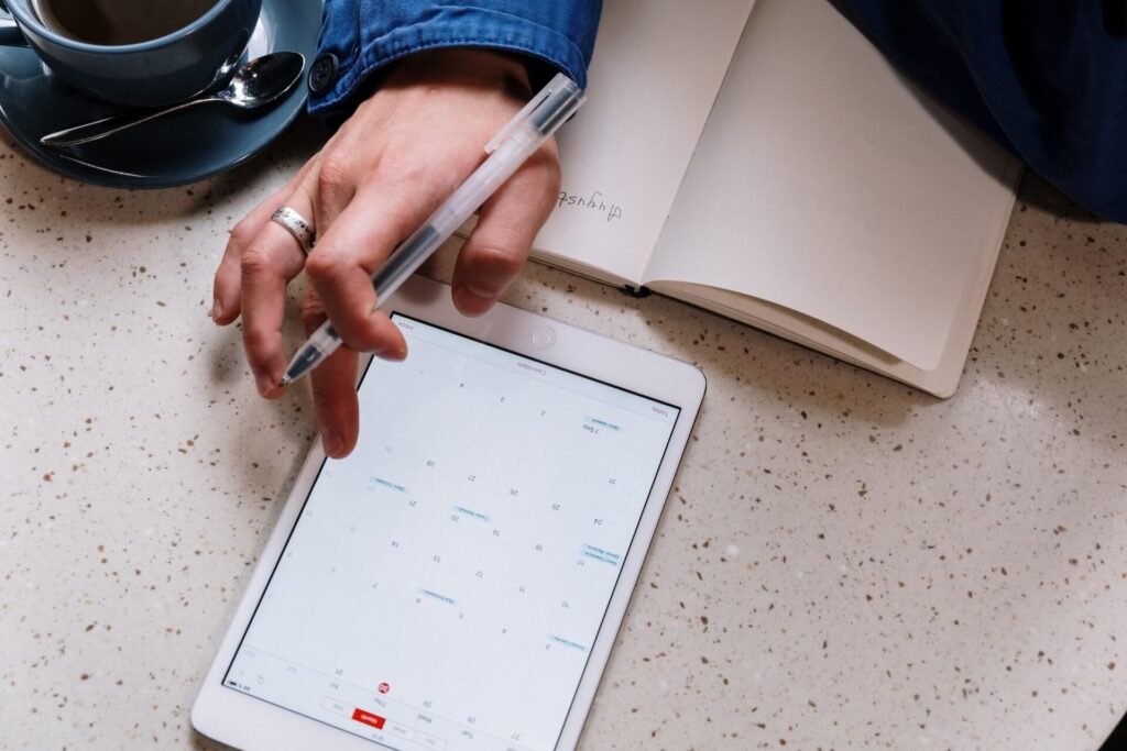 hand  holding pen with a tablet showing calendar on the table