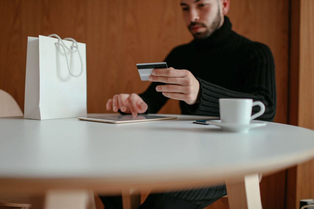 man holding credit card while using tablet 