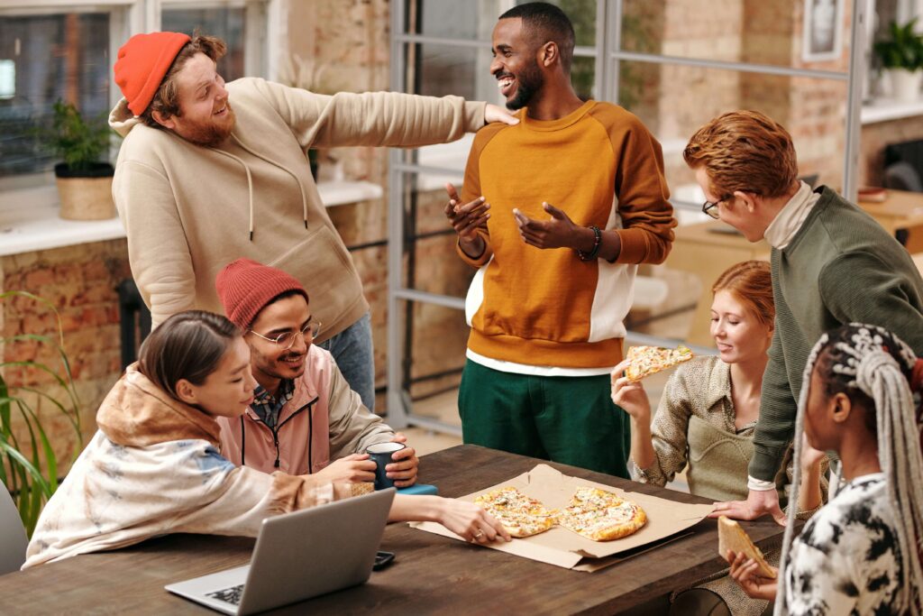 group of people talking while eating pizza with laptop on table