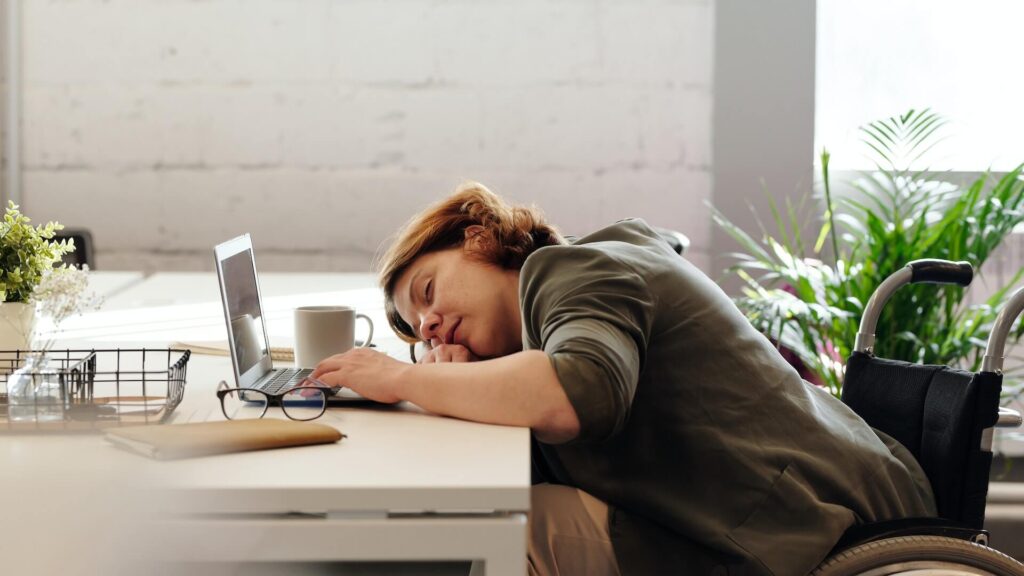 Woman sleeping on table with an open laptop and coffee mug