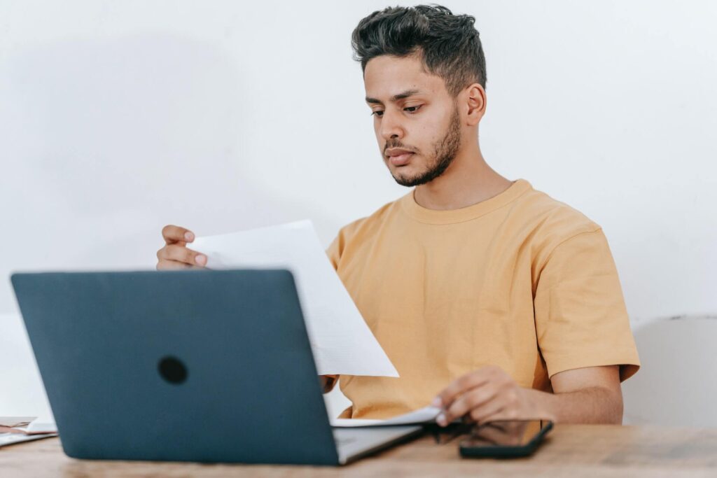 Man looking at documents while using a laptop