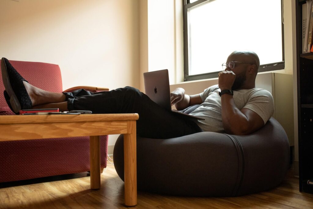 Man sitting on bean bag using a laptop, feet propped up on a coffee table