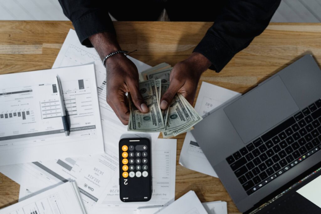 man counting money with laptop, calculator and papers on table