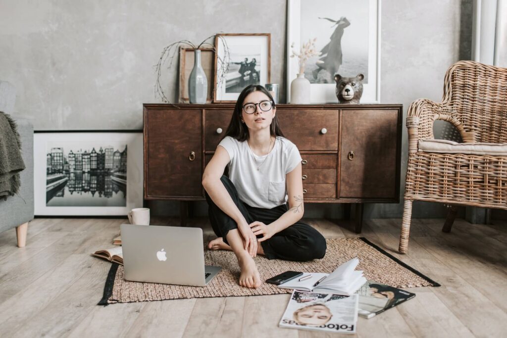 Woman sitting on floor surrounded by a laptop, books, a notebook, and magazines