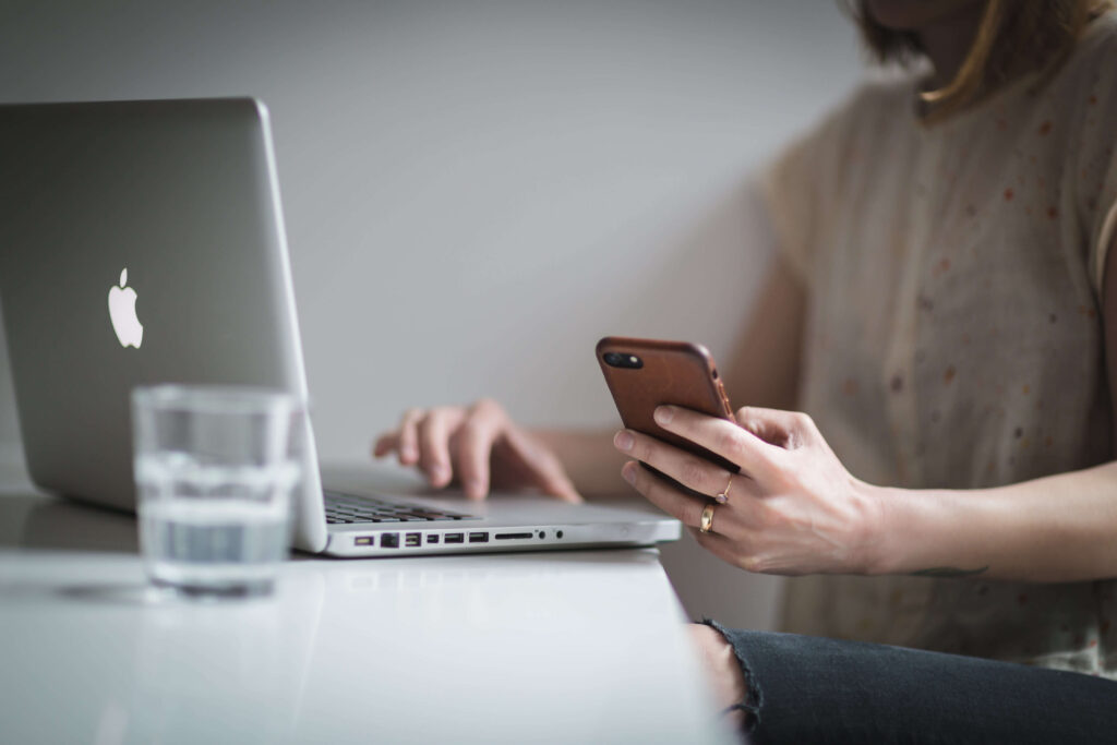 woman holding phone and scrolling on laptop